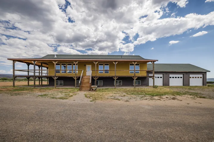 Expansive property featuring a raised exterior, a wraparound covered porch, and a dedicated multi-bay garage