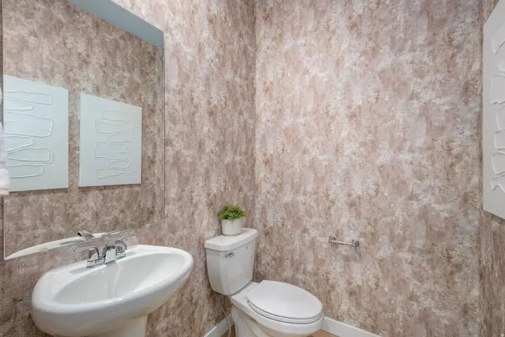 Pedestal sink with chrome faucet hardware, set against textured wallcovering
