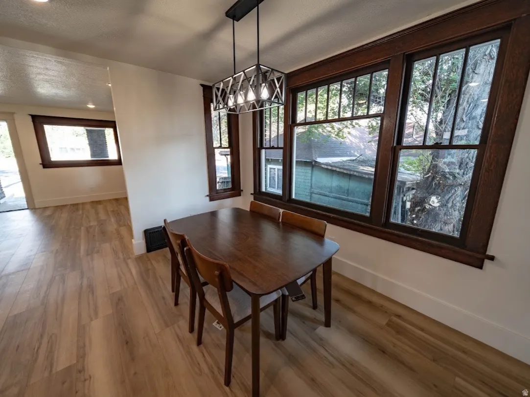Dining area featuring a wood-finish dining table with complementary chairs, hardwood flooring throughout, and abundant natural light from large multi-pane windows with wood framing