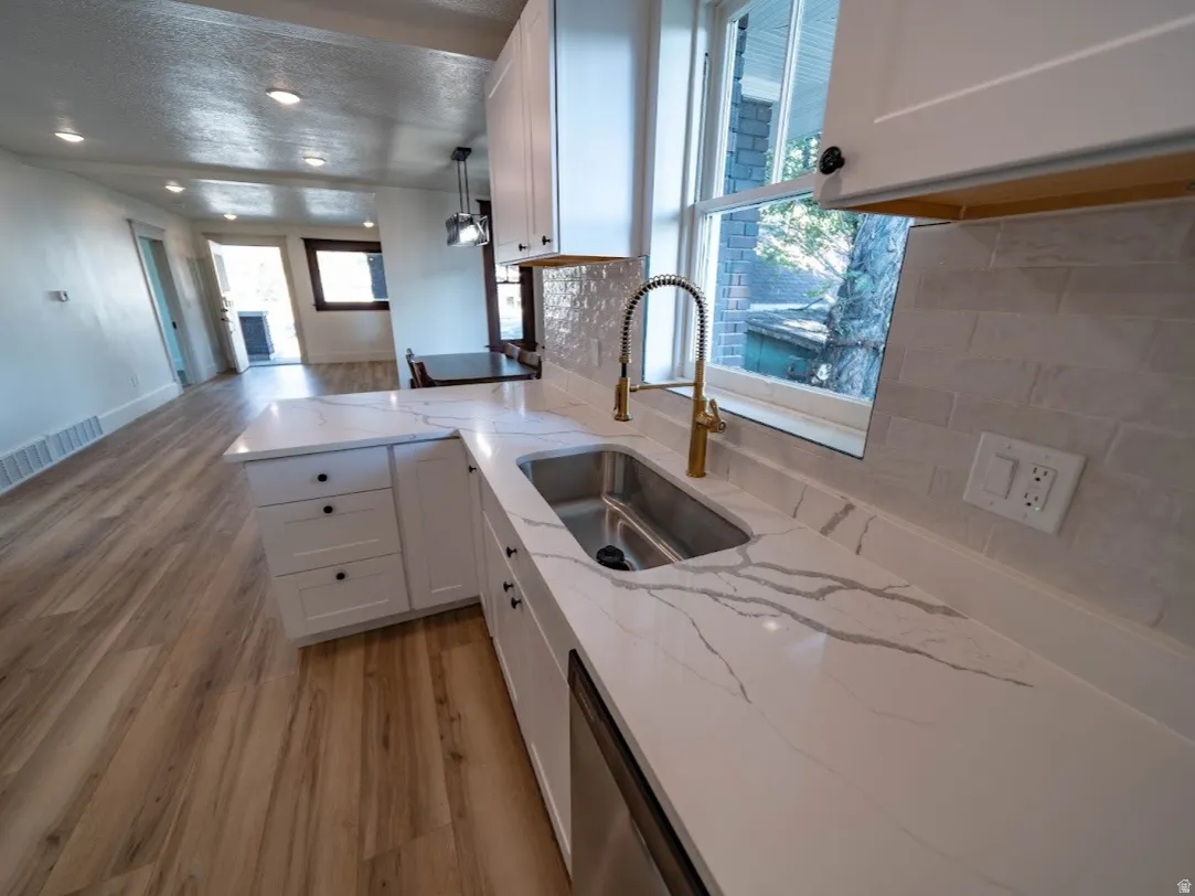 Modern kitchen featuring white cabinetry, a stainless steel undermount sink, a gold-toned pull-down faucet, light-toned stone-finish countertops with natural veining, and a white subway tile backsplash