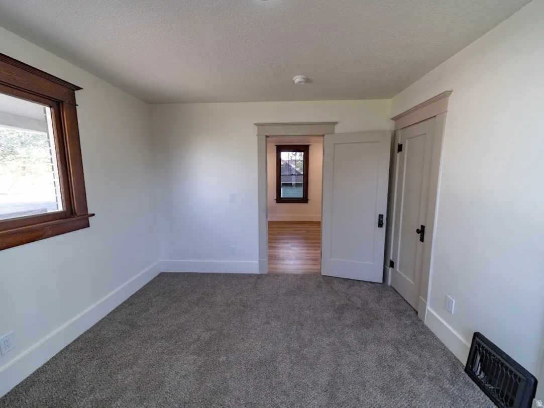 Carpeted interior space with light-toned walls, contrasting wood-trimmed window, and white baseboards