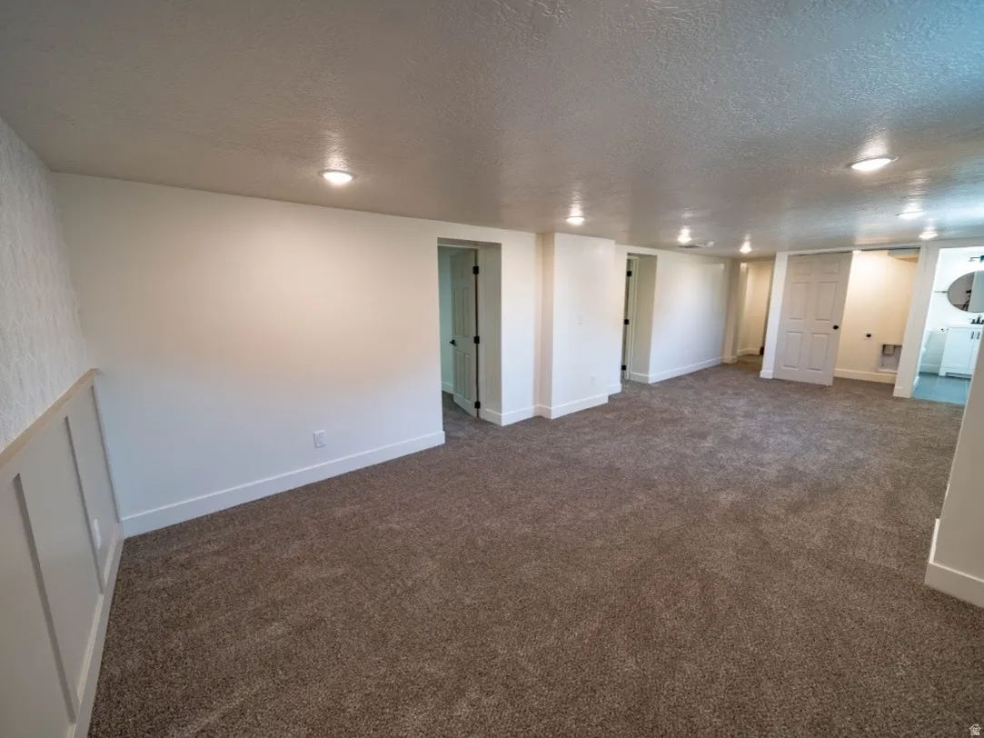 Spacious room featuring new carpeting, recessed lighting, white walls, and a decorative accent wall with wainscoting detail.  Laundry area is located in the closet