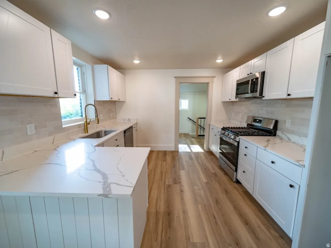 Modern kitchen featuring white shaker cabinetry, quartz countertops, stainless steel appliances, a tile backsplash, and wood-finish flooring