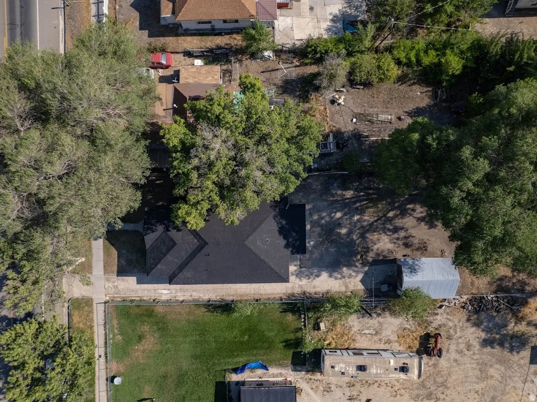 Property featuring a dark shingle roof, mature trees, a detached outbuilding with a metal roof, and a gravel driveway