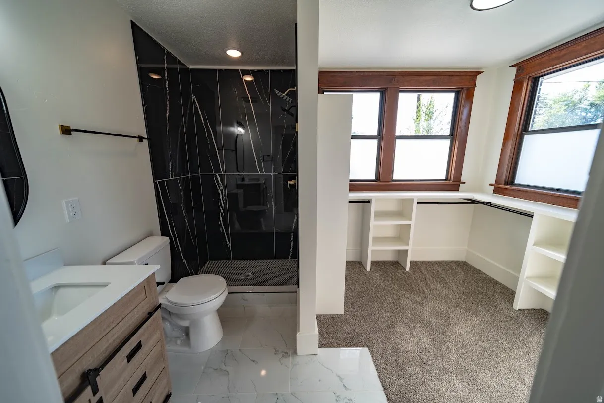 Luxurious bathroom featuring a walk-in shower with black tile surround, a wood-finish vanity with white countertop, and white marble-look floor tile