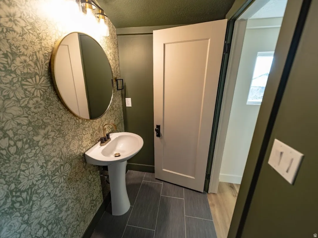 Pedestal sink with gold-finish faucet, framed by floral-patterned wallpaper and dark green walls