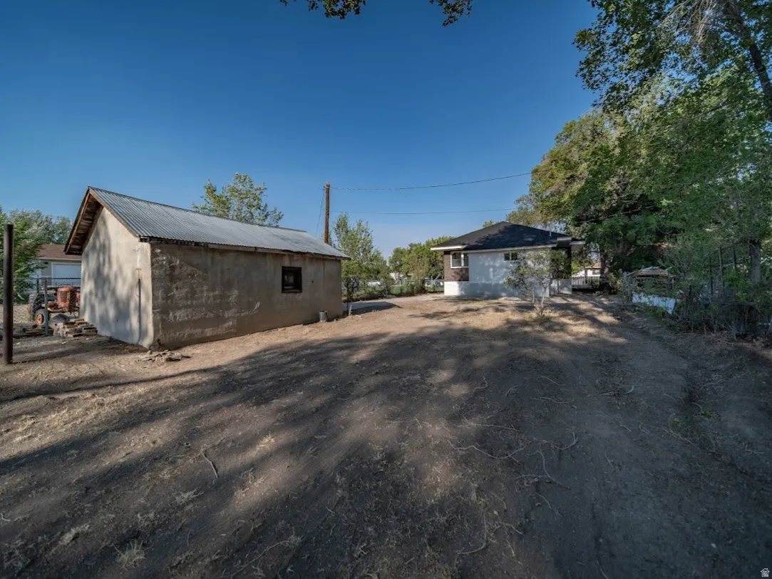 Detached single car garage with corrugated metal roof and stucco exterior, accompanied by a residential structure featuring a dark shingle roof and light-colored siding