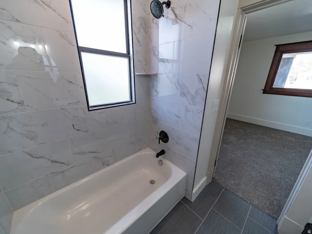 White bathtub with black fixtures, surrounded by large format white and gray veined tile