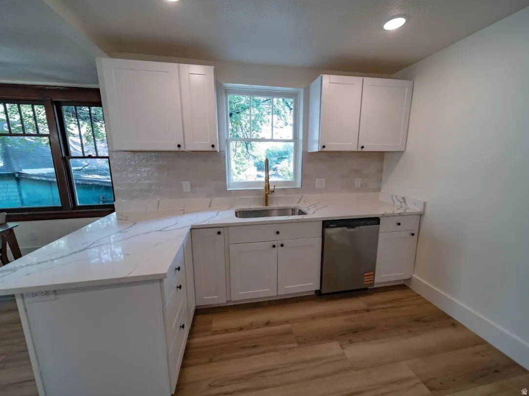 Modern kitchen featuring white shaker cabinetry, quartz countertops, a tile backsplash, wood-finish flooring, and a stainless steel dishwasher
