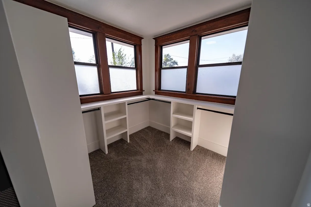 Bright corner office or den featuring multiple windows with wood-finish frames, abundant natural light, and built-in white cabinetry with shelving along two walls