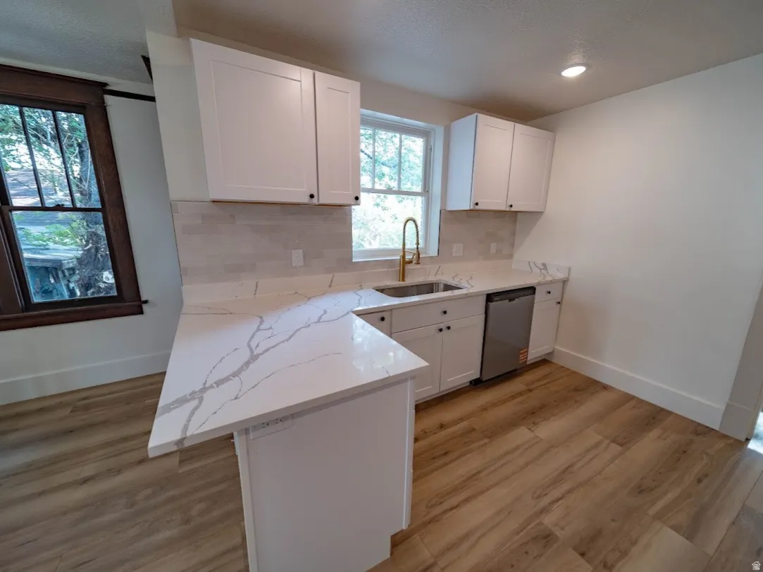 Kitchen featuring white shaker cabinetry, patterned stone countertops, a gold-toned faucet, and stainless steel dishwasher