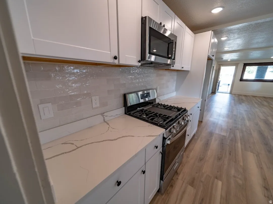 Modern kitchen featuring white shaker cabinetry, stainless steel appliances, a gas range, light-toned countertops with subtle veining, and a textured tile backsplash