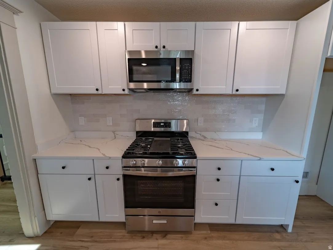 Kitchen featuring white cabinetry, light-toned countertops with veining, a stainless steel gas range, and a stainless steel microwave