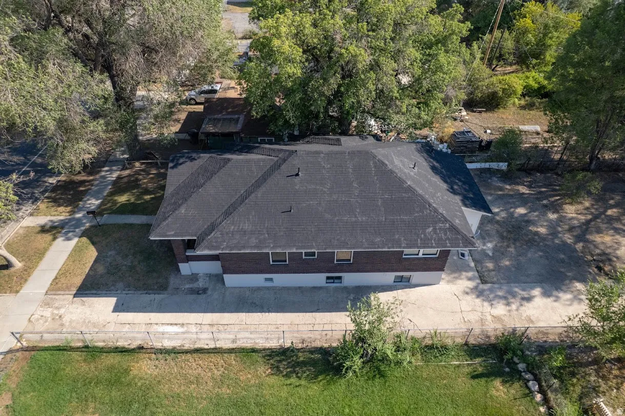 Pitched roof with dark shingles, perimeter fencing, mature trees, and a concrete pathway