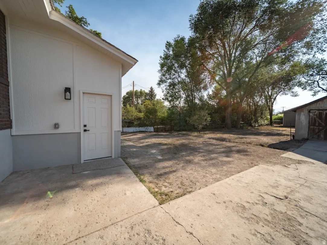 Concrete patio with an exterior entrance featuring a wall-mounted light fixture, brick detailing, and a separate structure with wooden doors