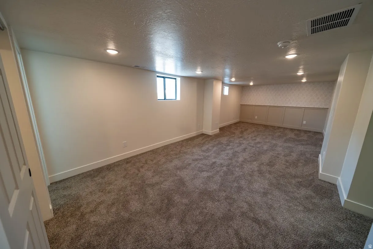 Spacious room featuring neutral carpeting, recessed lighting, white trim, and a decorative wainscoting wall accent