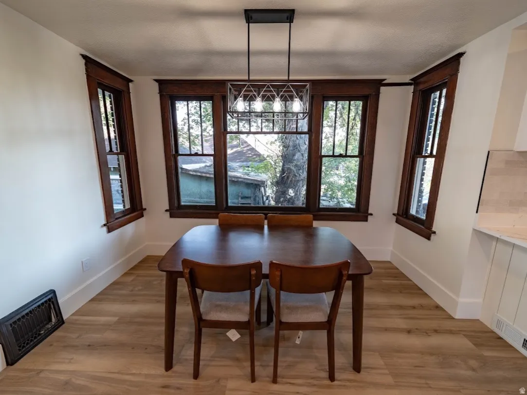 Dining space featuring wood-finish flooring, a modern geometric chandelier, and three large windows with dark wood trim