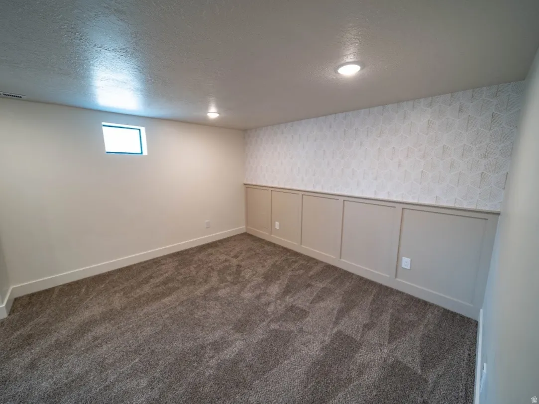 Carpeted room featuring a single window, recessed lighting, white baseboards, and a wall with geometric-patterned wallpaper above wainscoting