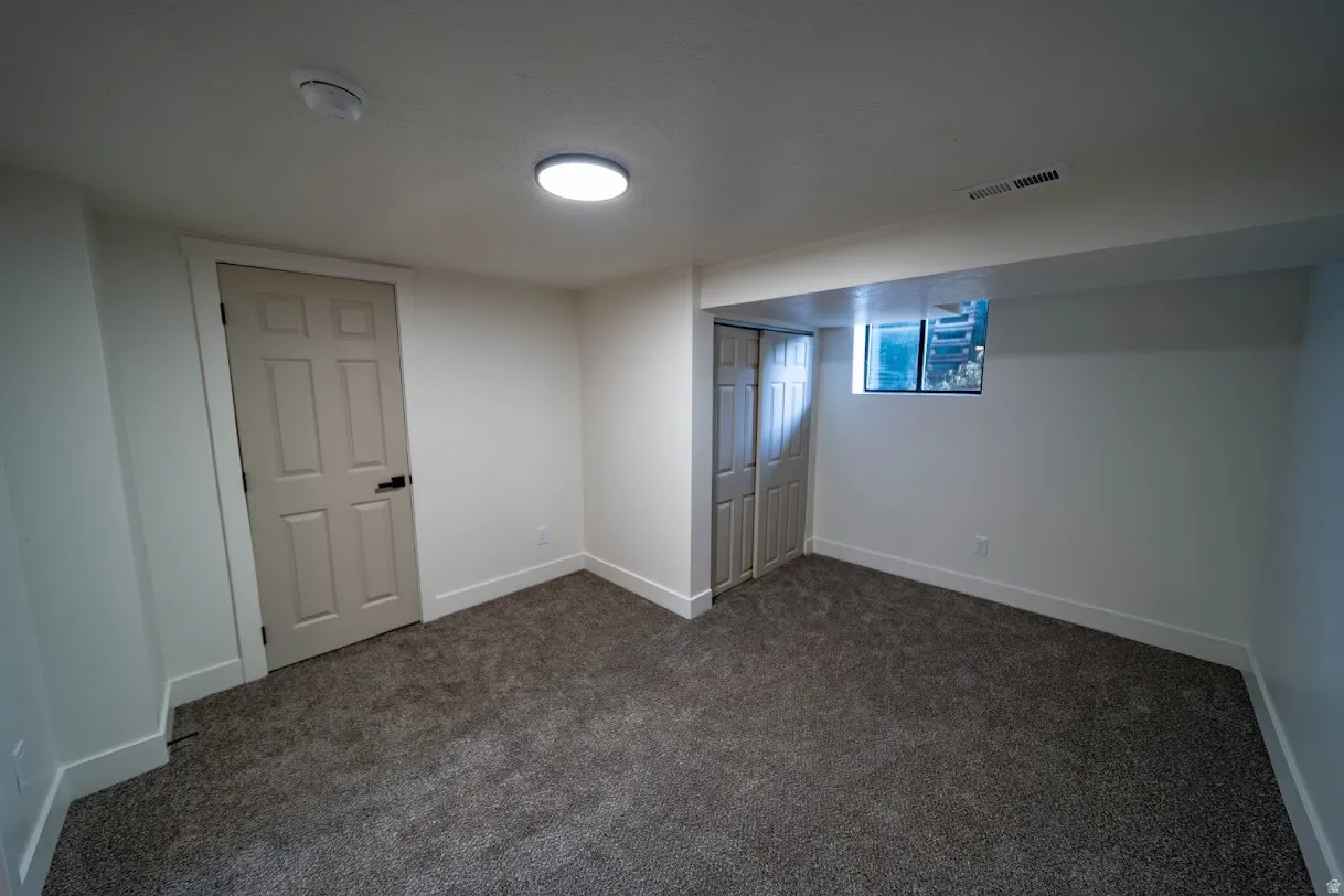 Room featuring plush gray carpeting, white walls, and a single flush-mount ceiling light