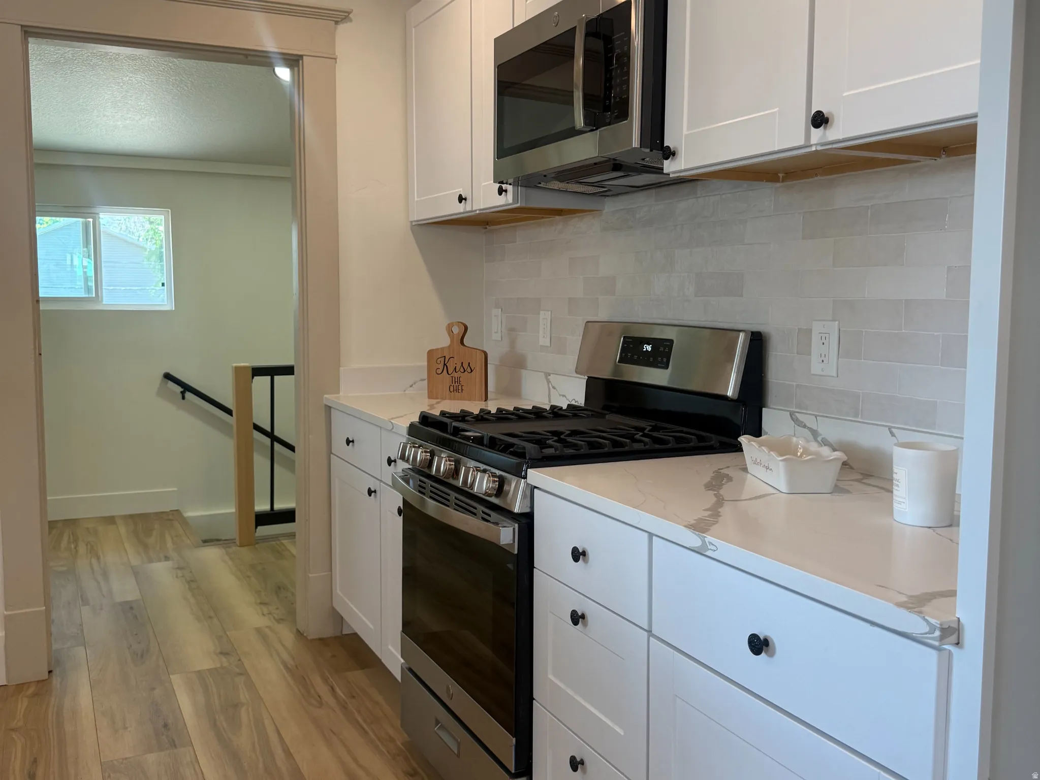 Modern kitchen featuring white shaker cabinetry with matte black hardware, stainless steel appliances, and wood-finish flooring