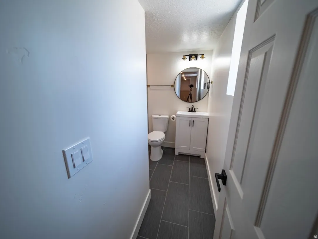 Bathroom featuring dark gray rectangular floor tiles, a white vanity with double doors, a circular mirror, and a three-light fixture with black accents.  Bathroom is located next to the laundry area.
