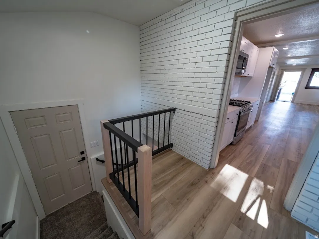 Bright hallway featuring white painted brick walls, wood-finish flooring, and black metal stair railing with clean lines.  Stairs going to the basement area and back door to the back yard.