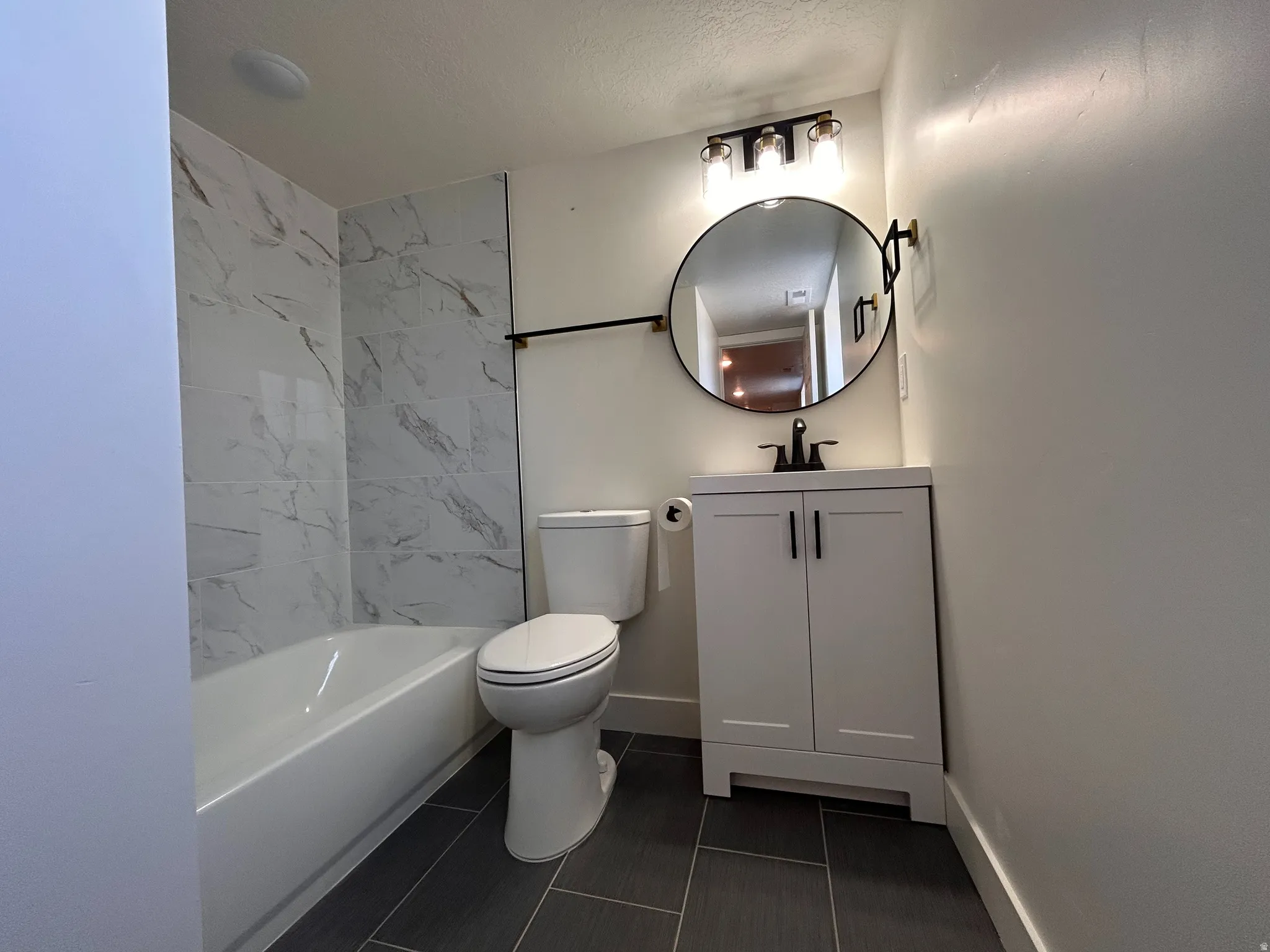 Contemporary bathroom featuring a white vanity with black hardware, a round black-framed mirror, and a three-light fixture with clear glass shades
