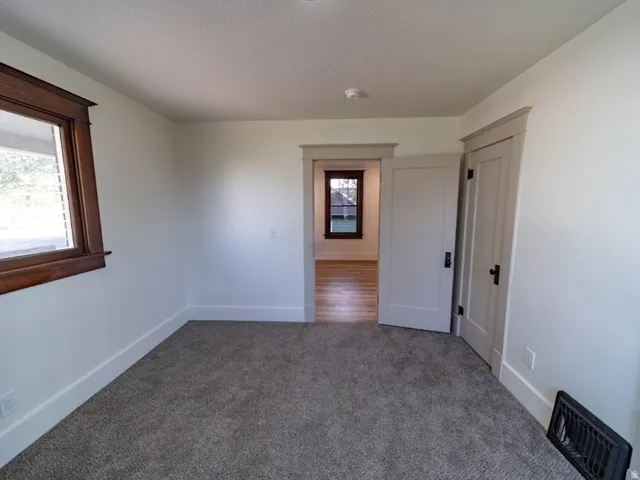 Carpeted interior space with light-toned walls, contrasting wood-trimmed window, and white baseboards