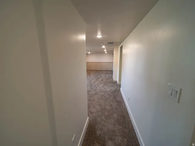 Carpeted hallway leading to an interior space featuring recessed lighting, light-toned walls, and white baseboards