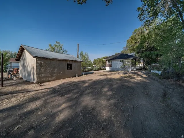 Detached single car garage with corrugated metal roof and stucco exterior, accompanied by a residential structure featuring a dark shingle roof and light-colored siding