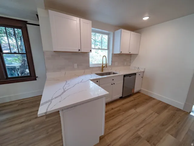 Kitchen featuring white shaker cabinetry, patterned stone countertops, a gold-toned faucet, and stainless steel dishwasher