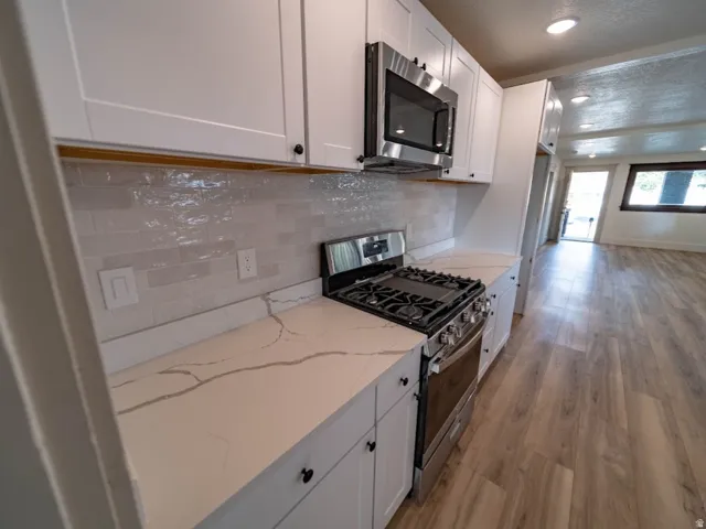 Modern kitchen featuring white shaker cabinetry, stainless steel appliances, a gas range, light-toned countertops with subtle veining, and a textured tile backsplash