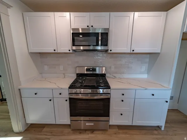 Kitchen featuring white cabinetry, light-toned countertops with veining, a stainless steel gas range, and a stainless steel microwave