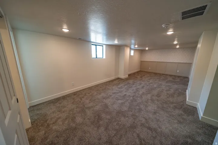 Spacious room featuring neutral carpeting, recessed lighting, white trim, and a decorative wainscoting wall accent
