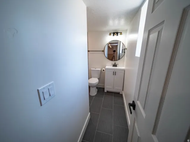 Bathroom featuring dark gray rectangular floor tiles, a white vanity with double doors, a circular mirror, and a three-light fixture with black accents.  Bathroom is located next to the laundry area.