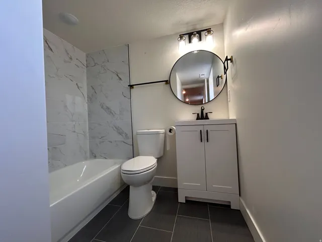 Contemporary bathroom featuring a white vanity with black hardware, a round black-framed mirror, and a three-light fixture with clear glass shades