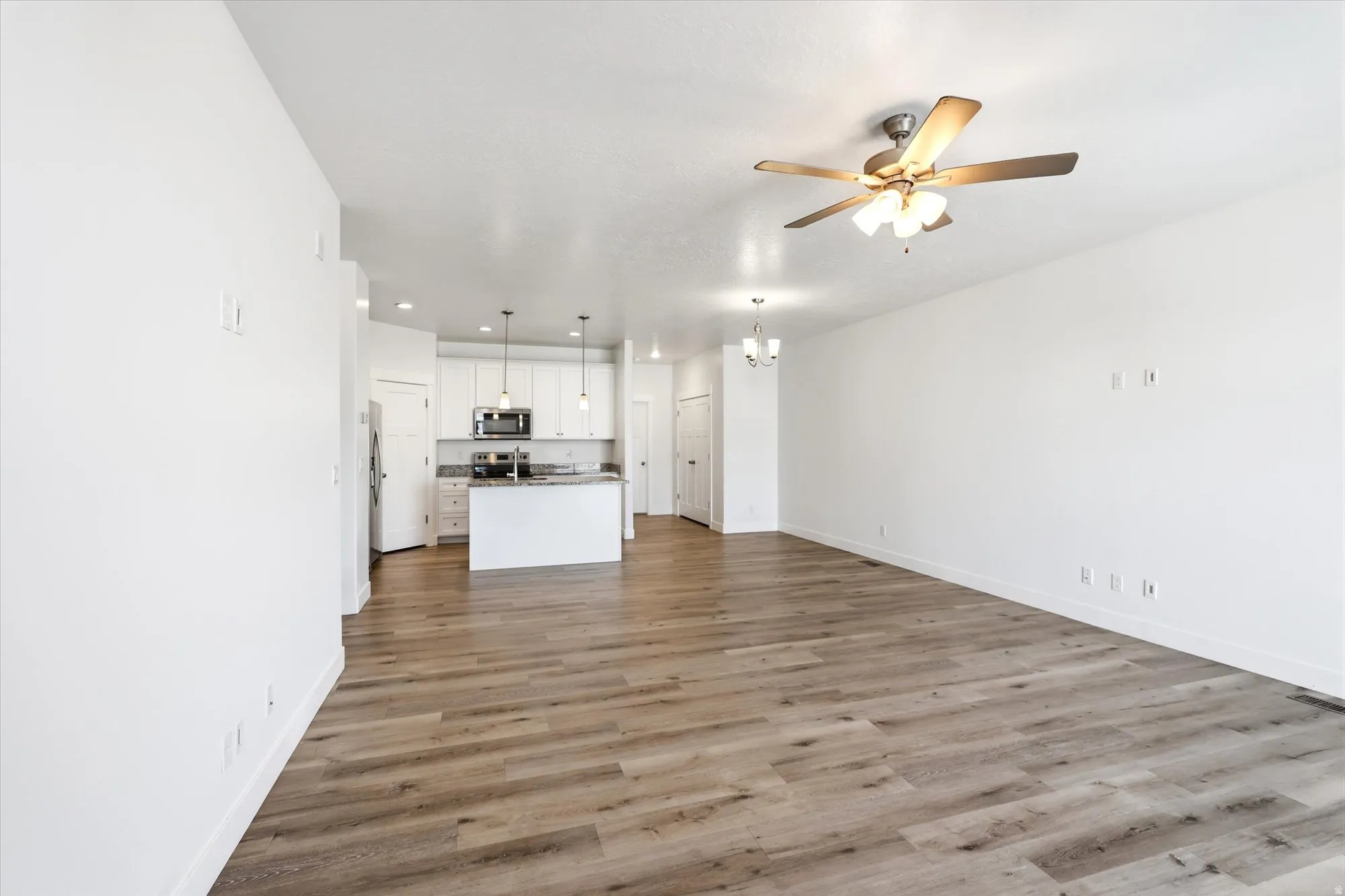 Spacious open-concept interior featuring wood-finish flooring, a ceiling fan with integrated lighting, recessed lighting, a white kitchen island, and stainless steel appliances