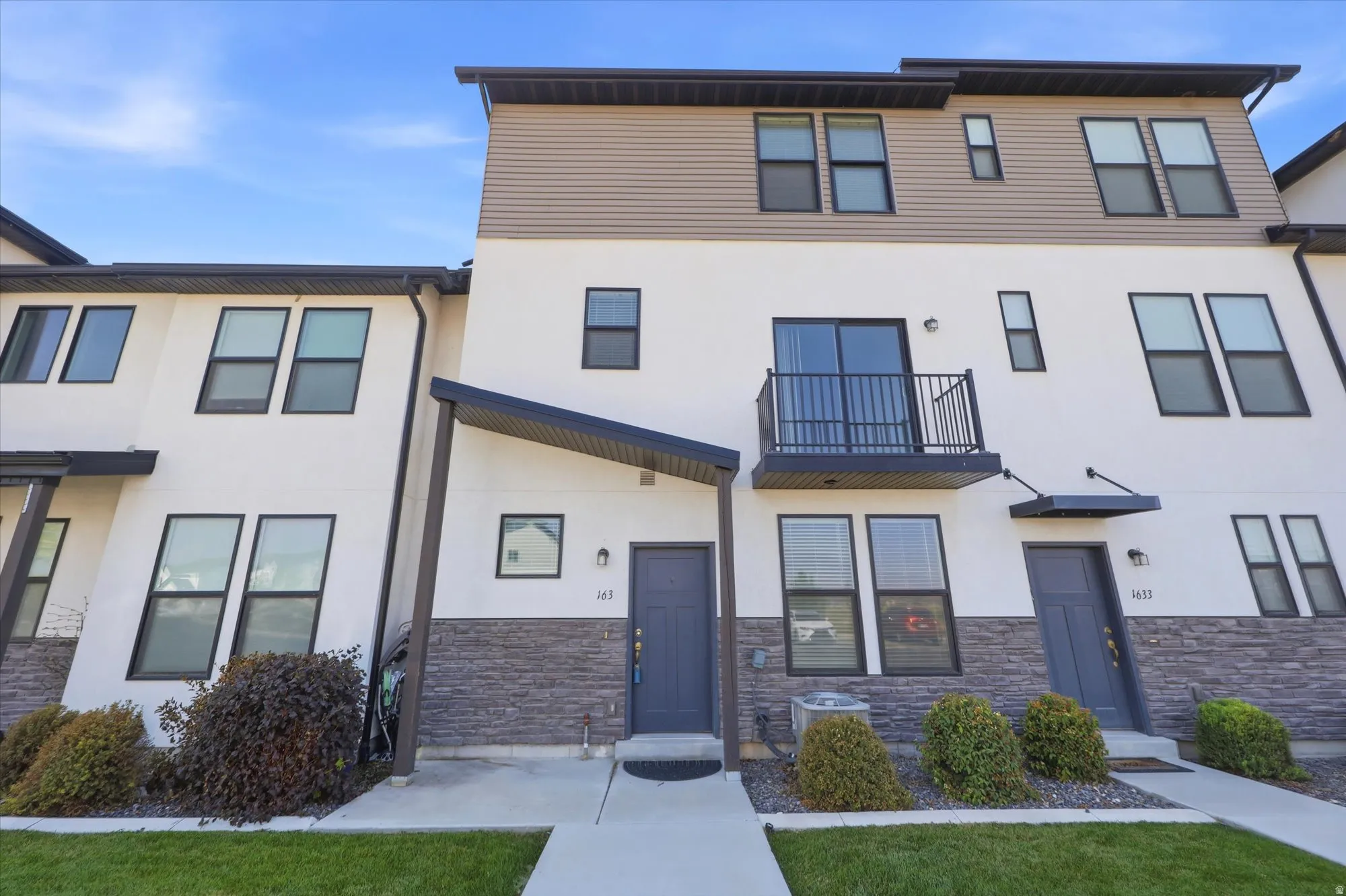 Modern multi-story townhouse exterior featuring white stucco and stone veneer accents