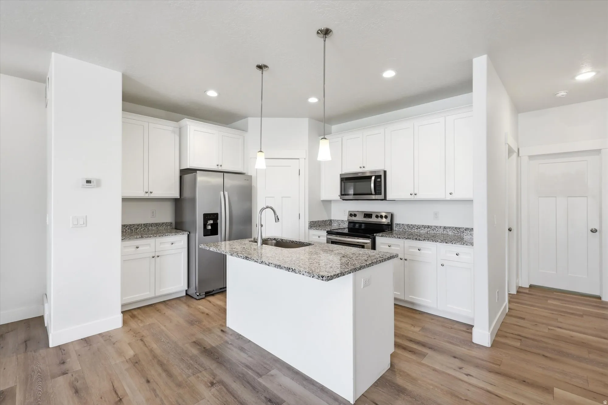 White shaker cabinetry with granite countertops, stainless steel appliances, a central island, recessed lighting, and wood-finish flooring
