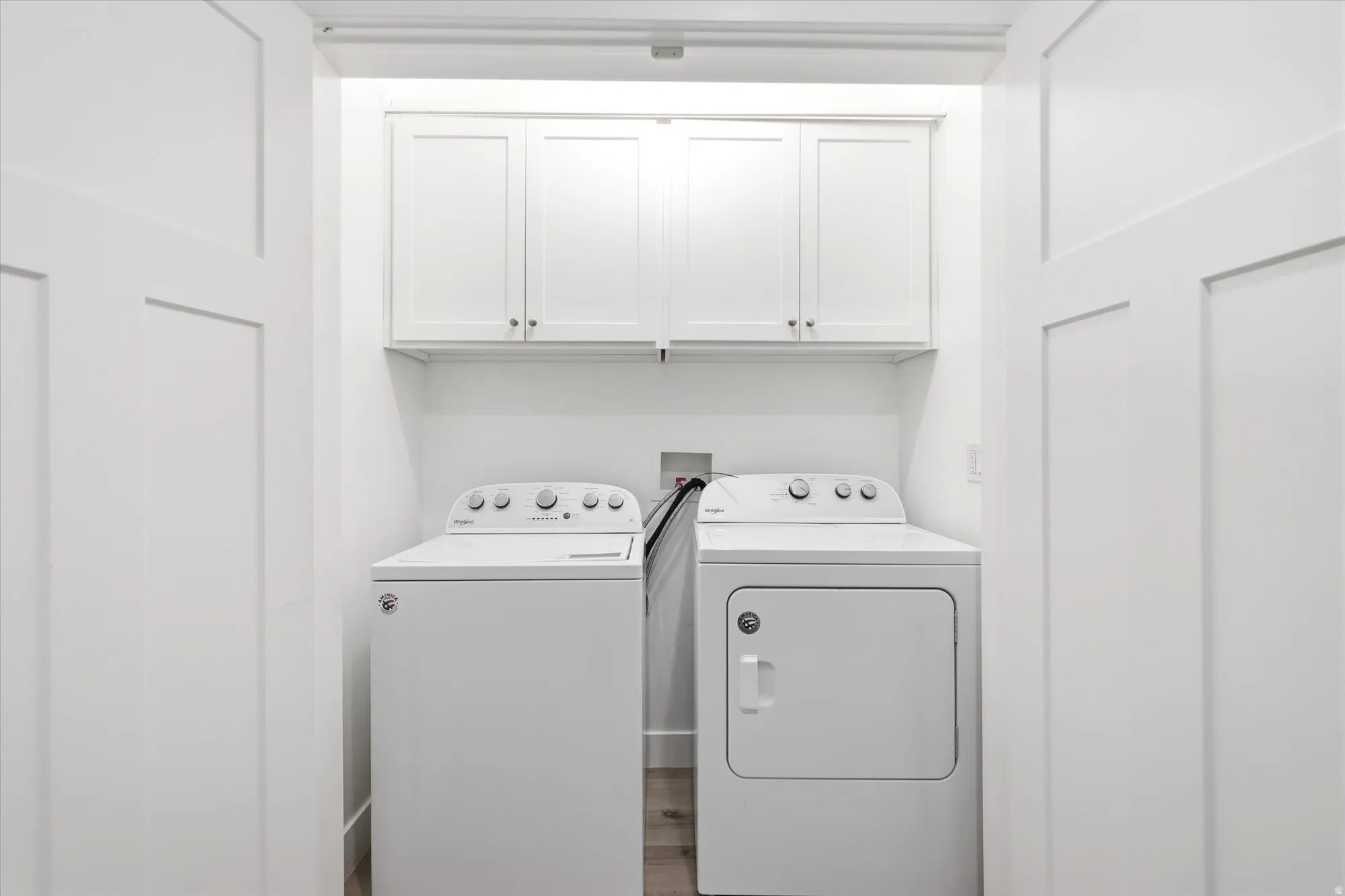 Dedicated laundry area featuring overhead white shaker cabinetry and wood-finish flooring