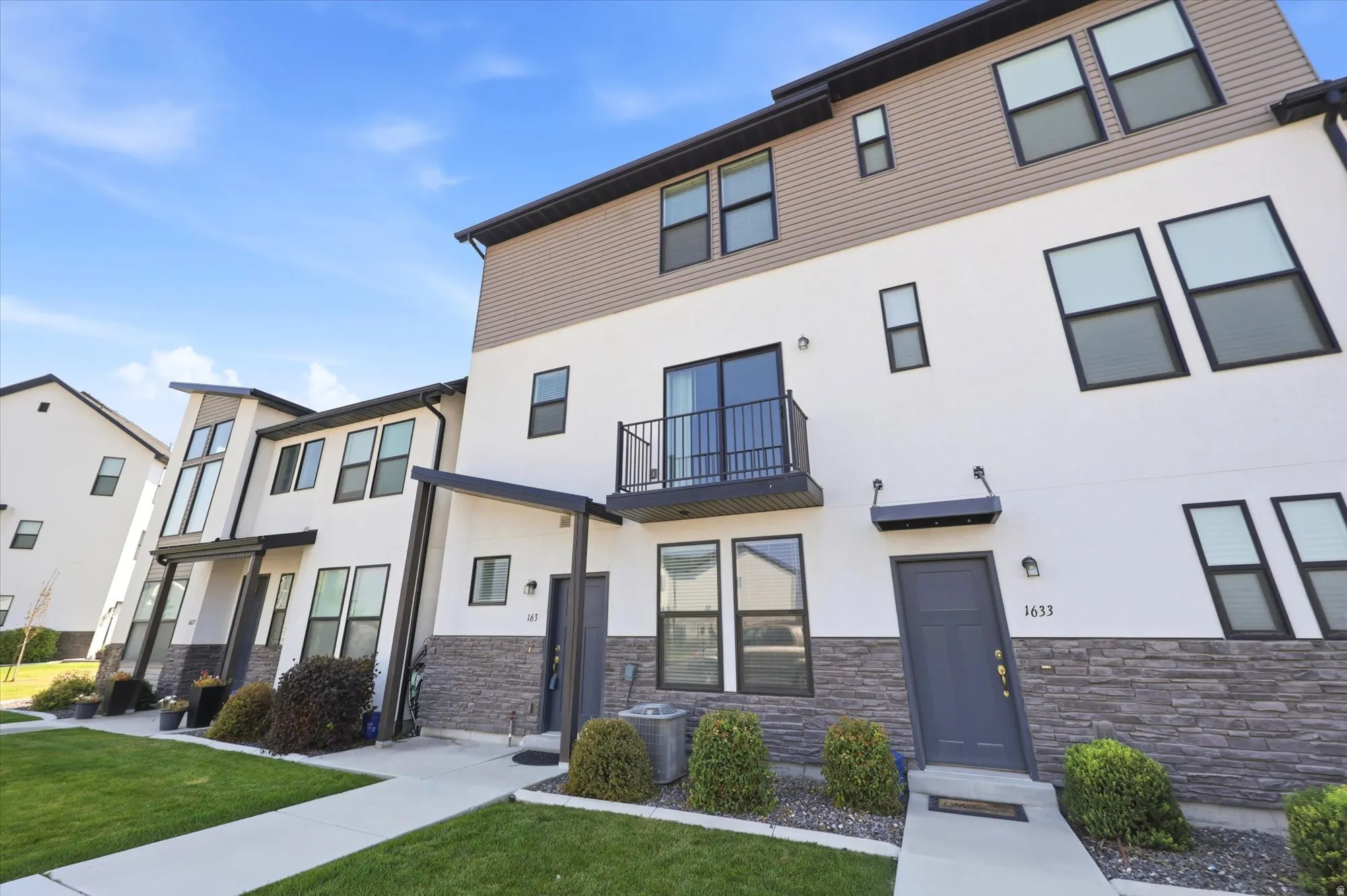 Contemporary townhome exterior featuring white stucco, horizontal siding, and stone veneer accents