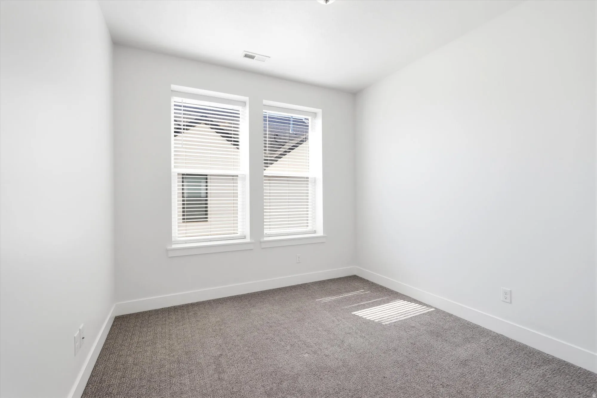 Bright room featuring two windows with white horizontal blinds, light gray carpet, white walls, and white baseboards