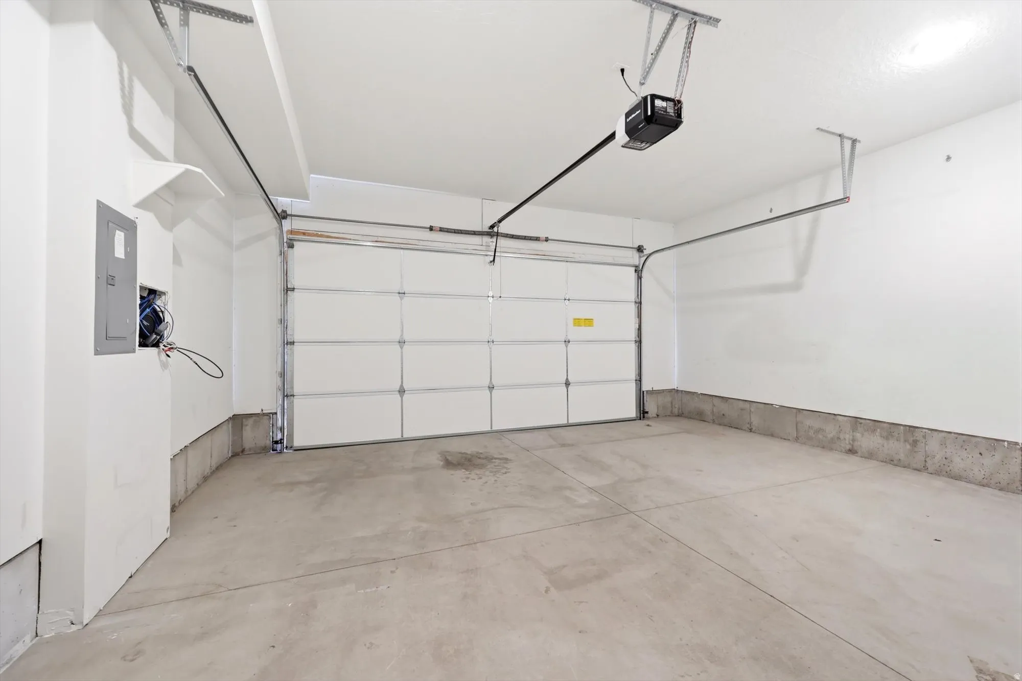 Spacious garage featuring a concrete floor, white painted walls, automatic garage door opener, and a panel box