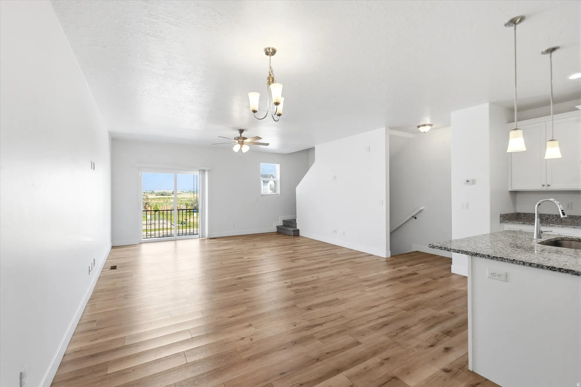 Open-concept living area featuring wood-finish flooring, a sliding glass door to a balcony, a ceiling fan, and a kitchen island with a stone countertop and pendant lighting