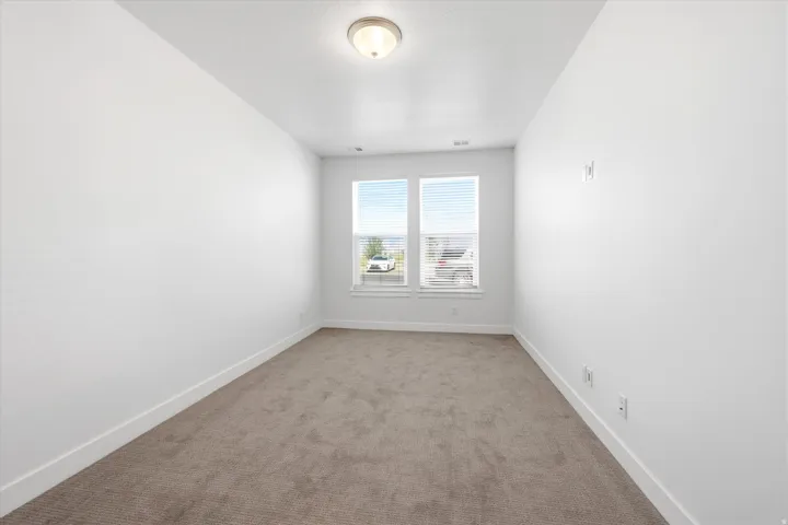 Carpeted interior room featuring two windows with horizontal blinds, white walls, and a ceiling-mounted light fixture