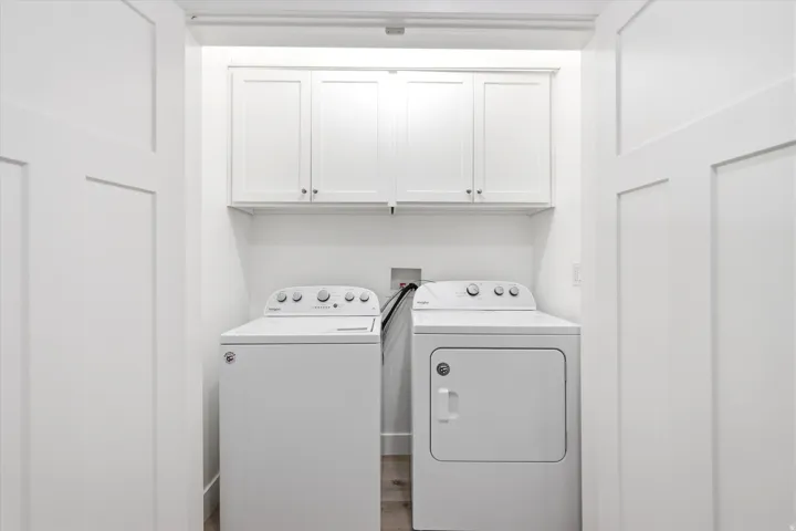 Dedicated laundry area featuring overhead white shaker cabinetry and wood-finish flooring