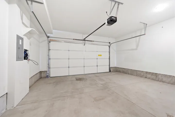 Spacious garage featuring a concrete floor, white painted walls, automatic garage door opener, and a panel box
