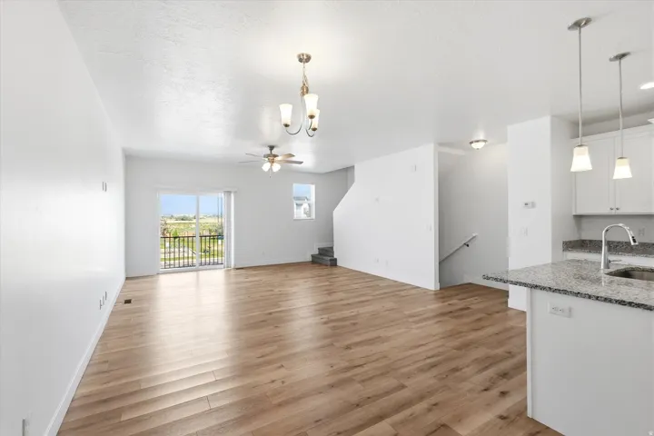 Open-concept living area featuring wood-finish flooring, a sliding glass door to a balcony, a ceiling fan, and a kitchen island with a stone countertop and pendant lighting