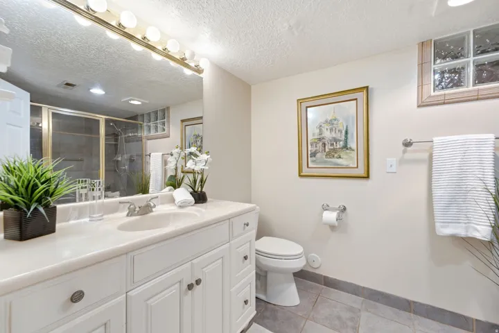 White vanity with an integrated sink and ample storage, large wall mirror, and a glass-enclosed shower