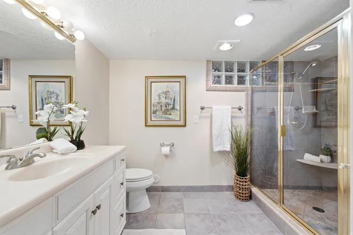 Vanity with a single basin sink, gold-framed shower enclosure, glass block window, and tile flooring